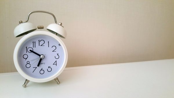 A white, analog alarm clock sits on a white table with a white background